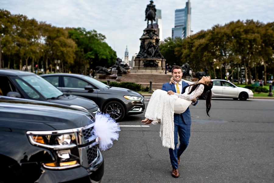 A Groom carries his bride across the street through traffic in Philadelphia.